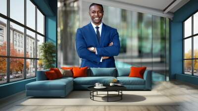 Smiling african american businessman CEO standing proud with arms crossed outside office workplace, colorful, reflective glass building, copy space Wall mural