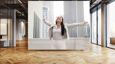 Victorious hispanic business woman raising her arms up to the sky, celebrating her success and achievements for her new career Wall mural