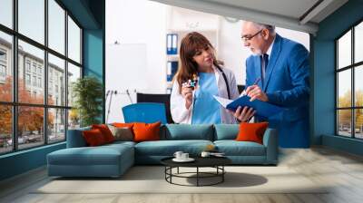 Old businessman visiting young female doctor Wall mural