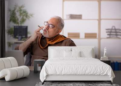 Old male employee smoking cigarette at workplace Wall mural