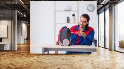 Young male contractor repairing vacuum cleaner at workshop Wall mural