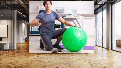 Young male employee exercising in the office Wall mural