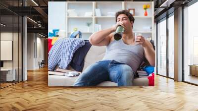 Young man student drunk drinking alcohol in a messy room Wall mural