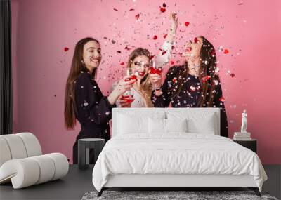 Three women celebrate the New Year party having fun laughing under the flying confetti and drinking wine. Wall mural