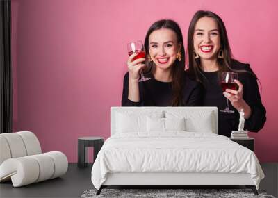 Two beautiful girls twins celebrate successful completion of the project and drinking wine. indoors party, smile girls wearing black stylish evening outfits. Indoors party, smile girls wearing black s Wall mural