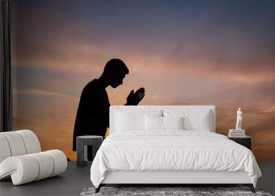 Silhouette of a person praying at sunset with vibrant skies and mountains in the background Wall mural