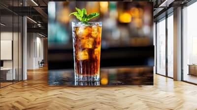 A close-up shot of a glass filled with a Long Island Ice Tea cocktail, garnished with a sprig of mint, resting on a bar counter.  Wall mural