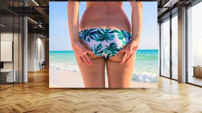 Woman in bikini stands on white sand beach in front of turquoise blue sea. Wall mural