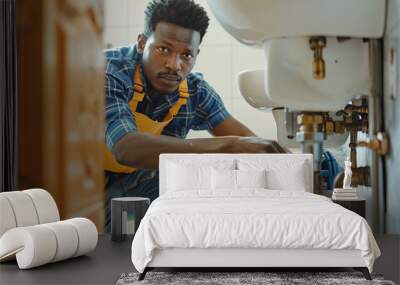 Young Black male plumber working on fixing a bathroom sink while seated on the floor, viewed from the doorway Wall mural