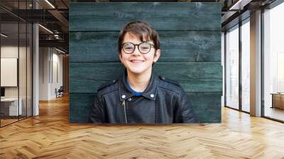 portrait of 12 year old boy with glasses smiling on green wood background dressed in leather jacket Wall mural