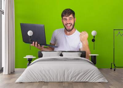 Image of happy excited young man posing isolated over green wall using laptop computer make winner gesture. Wall mural