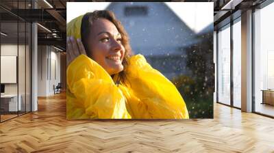 Young happy woman wearing yellow raincoat is feeling free and smiling under the rain. Concept of life, freedom, nature, adventure, purity. Wall mural