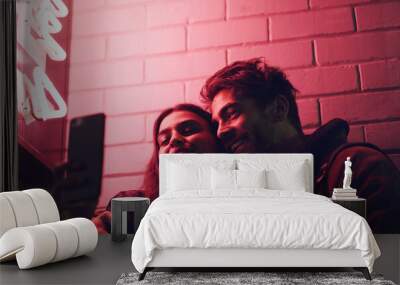 This is a night to remember. Shot of a young couple taking a selfie while standing outside a building at night. Wall mural