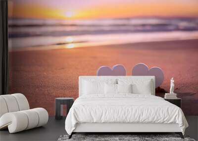 Two white hearts standing on the sand of a beach, illuminated by a beautiful sunset over the sea, creating a romantic atmosphere Wall mural