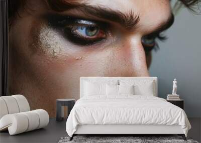 A close-up portrait of a man with bold eye makeup, including black eyeliner, gold glitter, and long lashes. Wall mural