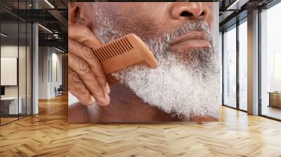 Senior man, hands and beard with comb in grooming, beauty or skincare hygiene against a studio background. Closeup of African elderly male face combing or brushing facial hair for clean wellness Wall mural