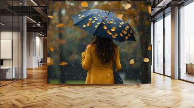 A woman in an elegant yellow coat walks through the rain, holding a black umbrella with small gold leaves on it Wall mural