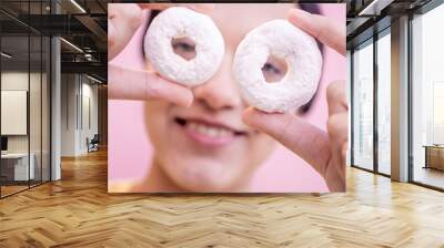 Latin woman holding two delicious donuts in front of her eyes with a pink background. Wall mural