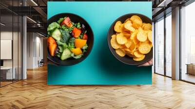 A person holding two bowls, one with fresh vegetables and the other filled with potato chips, illustrating the choice between healthy food or fast food Wall mural