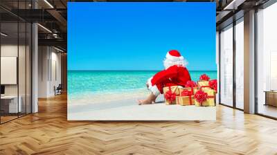 Christmas Santa Claus with gift boxes relaxing at ocean beach Wall mural