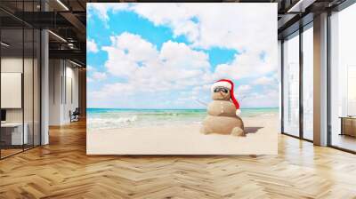 Sandy snowman in santa hat on sea beach. New Years and Christmas Wall mural