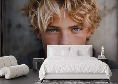 A close-up of a pensive teenage boy with messy blond hair and blue eyes, wearing a hoodie with a neutral backdrop. Wall mural