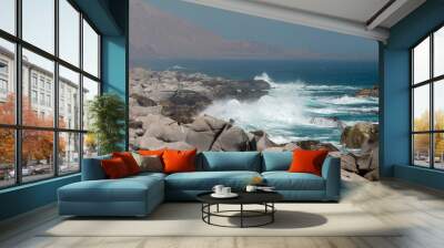 Turquoise waves crash on rocks with a hazy mountain range in the background on a sunny day, creating a peaceful, breathtaking landscape. Perfect for a tranquil summer adventure Wall mural