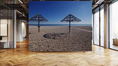 Deserted pebble beach and two umbrellas, in the background the blue sea and sky. Wall mural