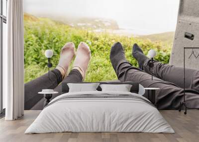 Photo of four legs with two reusable mugs on top of the sofa inside a campervan with its rear doors opened showing the views from the parking Wall mural