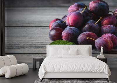 Plums on wooden table, harvested prune fruits green leaves in a pile closeup, copy space Wall mural