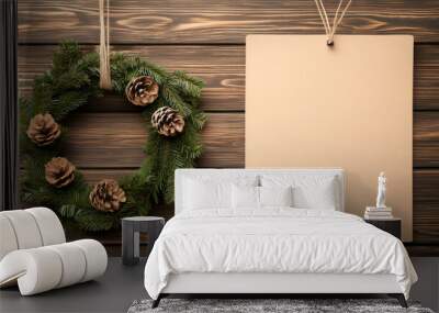 A beautiful Christmas wreath with pinecones, displayed next to a blank card on rustic wooden background. Perfect for holiday greeting. Wall mural