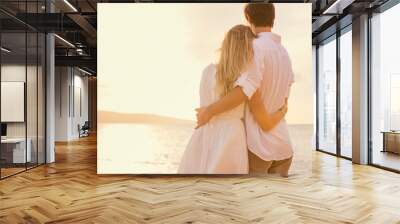 Happy romantic couple on the beach at sunset embracing each othe Wall mural