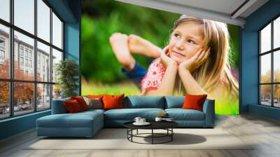 Portrait of a smiling little girl lying on green grass Wall mural