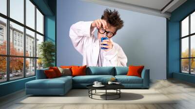 cool boy with wild hair and black glasses and white coat holds small bottle with blue liquid and looks like a mad scientist Wall mural