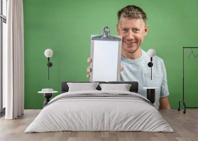 man with grey shirt is holding clipboard in front of green background Wall mural