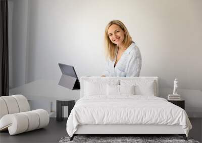 pretty young blonde business woman stands by her ergonomic height adjustable work desk and works on tablet from home in her home office Wall mural