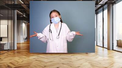 pretty young girl with 2 braids dressed as a doctor with protective mask and stethoscope in front of blue background Wall mural