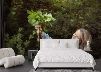 young blonde pretty woman with blue shirt and green apron harvesting white elongated icicle radishes from vegetable patch, high patch and is happy Wall mural