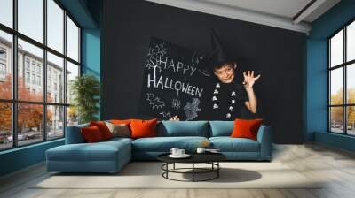 young boy dressed as a magician is holding happy halloween chalkboard in front of black background Wall mural