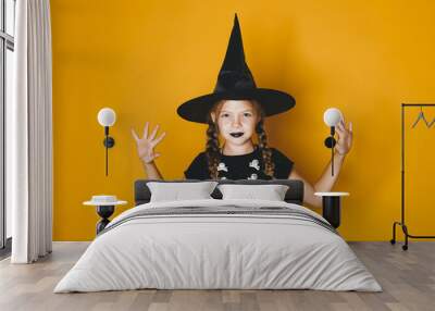 young halloween witch on orange background with black hat Wall mural