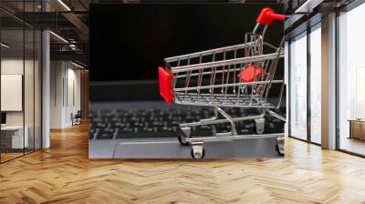 Small red shopping cart on silver laptop for shopping online with black screen background. Wall mural