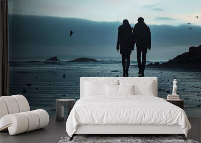 Silhouette of a young couple holding hands walking along the beach enjoying the beautiful sunset. Wall mural