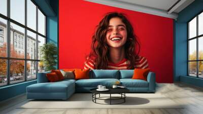 A cheerful teenage girl, laughing with delight, on a red solid background. Wall mural