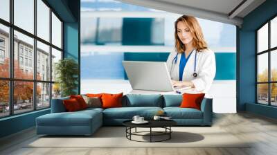 Attractive young woman doctor nurse practitioner physician assistant in hospital clinic medical office with laptop computer Wall mural