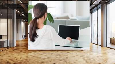 Rear over-the-shoulder view of young woman in home living waiting room lobby working on blank screen laptop computer Wall mural