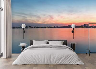 Panoramic shot of sunset over a city and a calm blue sea with cloudy orange blue sky Wall mural