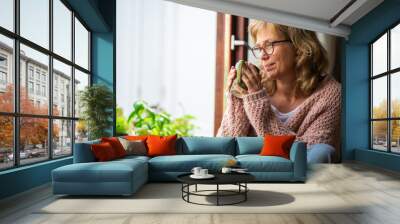 Adult woman taking tea pensive looking out the window Wall mural