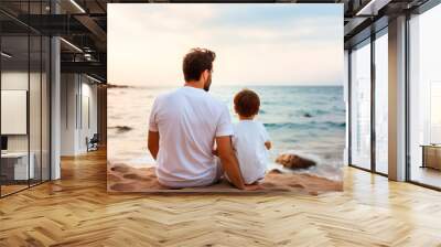 Father and son sitting on the beach looking at the sea at sunset, sharing a moment of calm. Wall mural