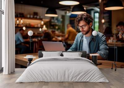 Focused man working on his laptop in a modern café with a cozy atmosphere. Wall mural