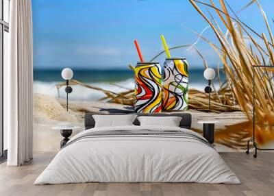 Two cans of soda with straws in them are on a beach Wall mural